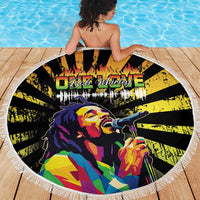 Round fringed beach blanket held on a deck, showing reggae singer portrait graphic