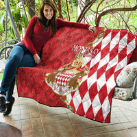 Red Monaco crest quilt blanket with diamond pattern and crown shield, draped on outdoor couch.