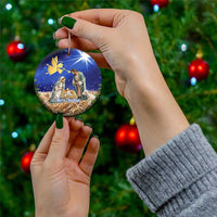 Blue ceramic round Christmas ornament with nativity scene, held by hand with gold string.