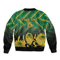 Green zip-up bomber jacket with black sleeves, "YOUR TEXT" 15 back print and gold protea graphic