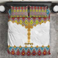 White bedding set with gold cross and colorful geometric tile pattern; two matching pillows.