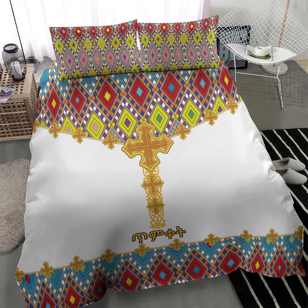 White bedding set with gold cross center and colorful diamond tile pattern border; two pillows.
