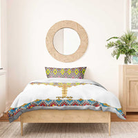 White duvet on bed with gold cross motif and colorful geometric tile border; one pillow.