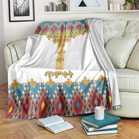White blanket with gold cross and multicolor diamond tile border, laid on sofa