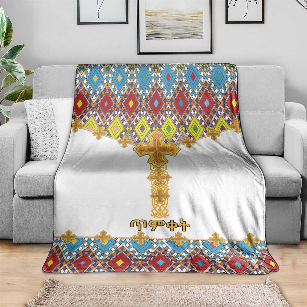 White cross-pattern blanket with gold Ethiopian cross and diamond tile hem on gray couch
