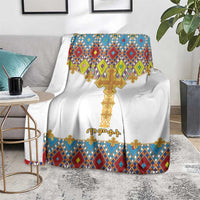 White cross-pattern blanket with gold cross and multicolor diamond border, on floor chair