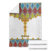 White blanket and folded stack with gold cross and multicolor diamond tile border