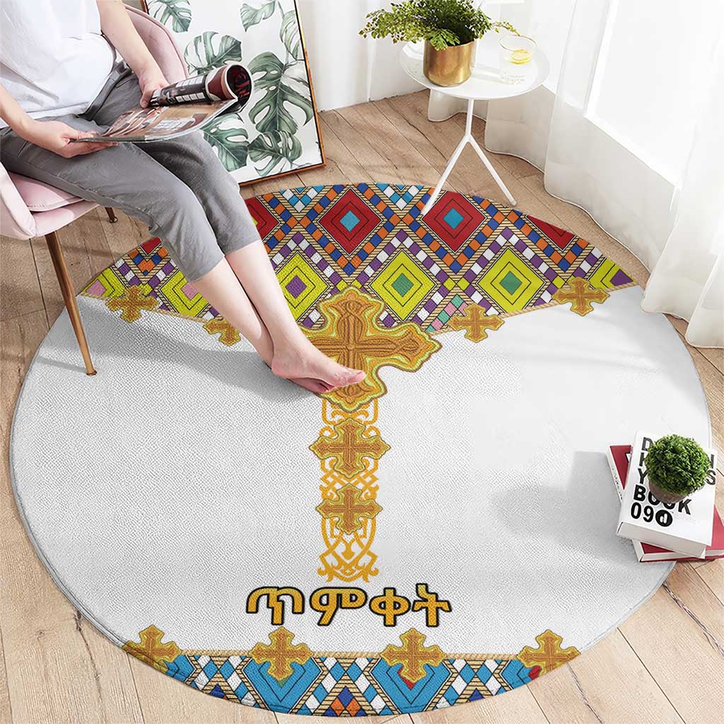 Round white area rug featuring a central gold cross with blue, green, purple tile shapes