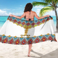 White sarong with colorful geometric tile pattern and gold cross emblem, draped wrap