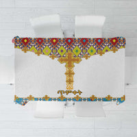 White tablecloth with colorful cross and geometric tile pattern, gold fringe edge