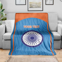Blue custom cricket blanket with orange edge, Indian emblem circle and 'YOUR TEXT' on sofa.