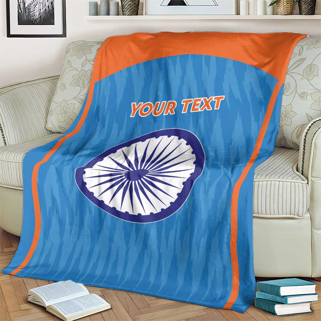 Blue cricket blanket with orange border, Indian emblem circle and 'YOUR TEXT' on armchair.