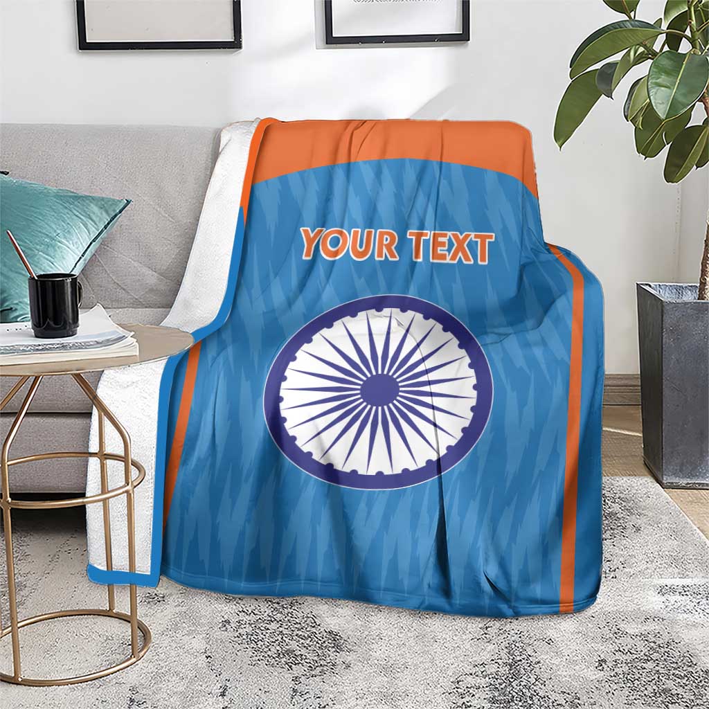 Blue cricket blanket with orange trim, Indian emblem circle and 'YOUR TEXT' on couch.