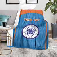 Blue cricket blanket with orange trim, Indian emblem circle and 'YOUR TEXT' on couch.