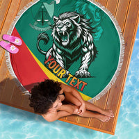 Round green beach blanket with fringed edge, lion and flag graphic, on striped mat