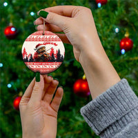 Hand holding a round red-and-white ceramic Christmas ornament with pine marten playing violin