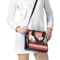 Red and black Christmas handbag with crossbody strap worn over white dress, front view