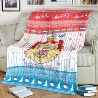 Christmas blanket with Luxembourg crest centerpiece and blue tree-pattern border on couch