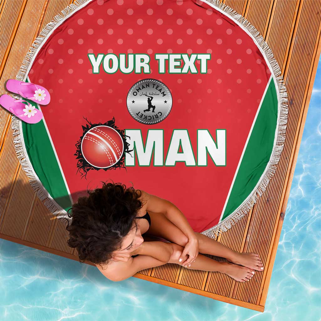 Red round beach blanket with green panel, printed Oman logo, and white tassel fringe