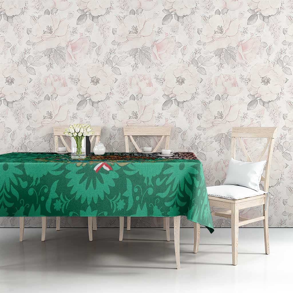 Green tablecloth with dense leaf print and red Aztec border, on dining table