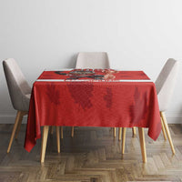 Red tablecloth with maple leaf pattern and dark center stripe on a dining table with chairs.