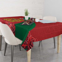 Red tablecloth with green drape and rose print, hanging over dining table edge.