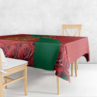 Red tablecloth with green panel and rose motifs on wooden dining table.