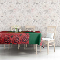 Red and green tablecloth with rose pattern and coat of arms on dining table.