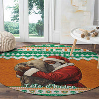 Round orange Christmas carpet with elephant hugging Santa, green border, placed on dark wood floor
