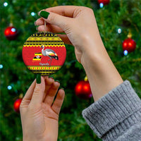 Round Uganda-themed Christmas ceramic ornament with grey crowned crane, held in hands.