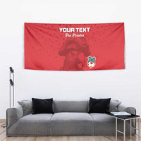 Red custom football tapestry with pirate graphic, crest, and “YOUR TEXT” text above gray couch.