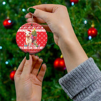 Red round ceramic ornament with alpaca holding gifts and a small Christmas tree; held by hand.