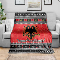 Red Christmas blanket over gray sofa, with Albanian eagle, festive icons, and black geometric trim