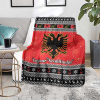 Red Christmas blanket on gray couch, showing Albanian eagle, black pattern stripes, Gezuar Krishtlindja
