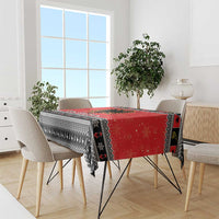 Red and black Christmas tablecloth draped over a dining table with patterned border.