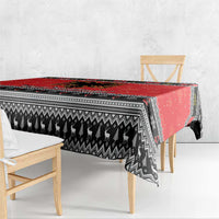 Red and black Christmas tablecloth hanging over table edge with patterned stripe border.