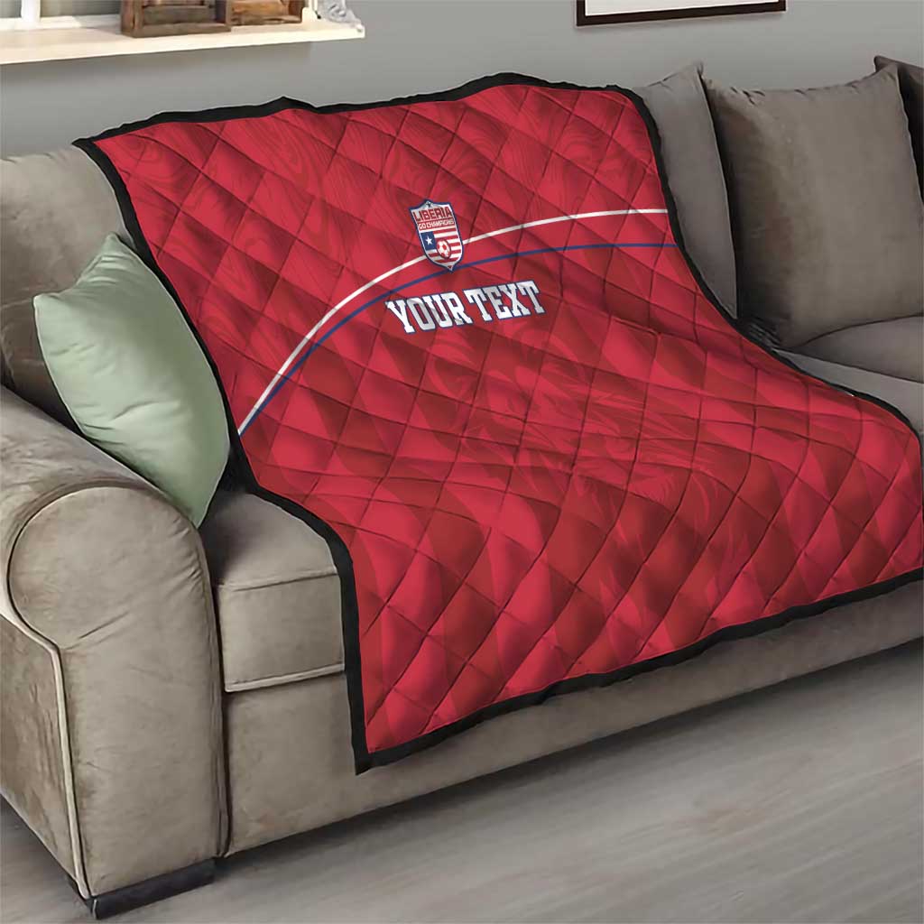 Red quilted football blanket draped on sofa with Liberia crest and 'YOUR TEXT' stripe.