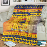 Christmas throw blanket draped on a couch, blue and gold crest with “Merry Christmas”