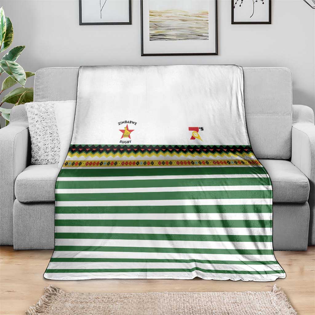 Folded rugby sevens blanket on sofa: white base, green stripes, patterned trim, logos