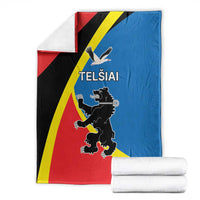 Folded red, blue, black, and yellow flag-themed blanket with Telsiai emblem, with white rolls