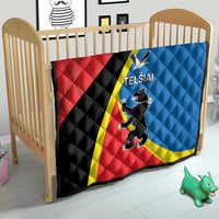 Red and blue quilt with yellow stripe and “TELSIAI” crest displayed on a crib bed