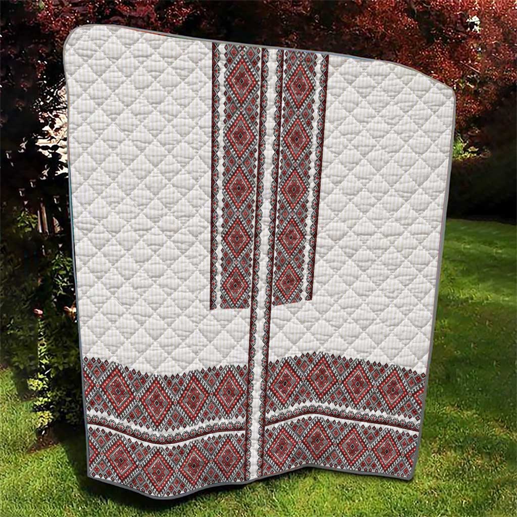 White quilt with red folk embroidery trim and diamond quilt stitching, angled view