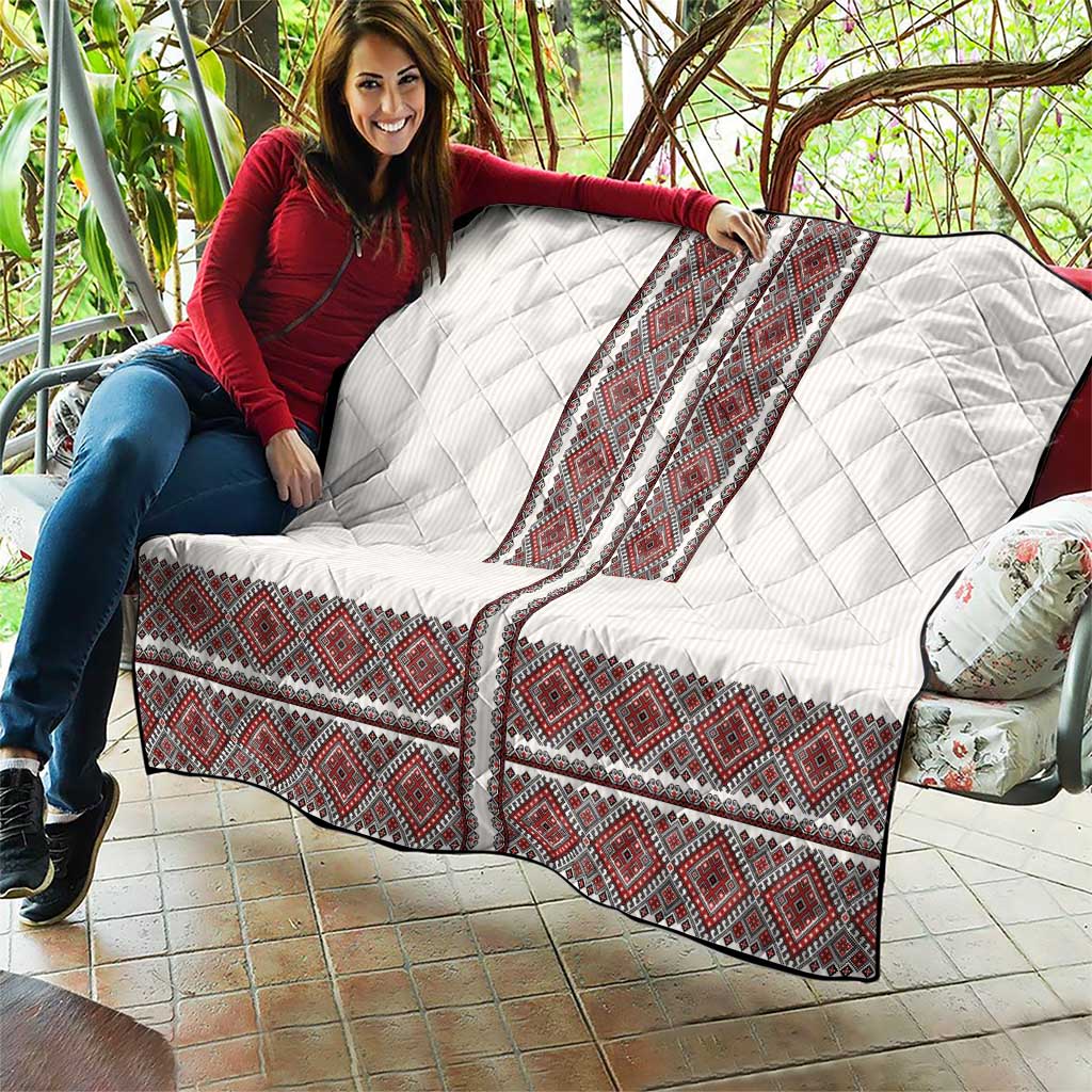 White quilt with red folk embroidery strips and diamond quilting, held on a patio