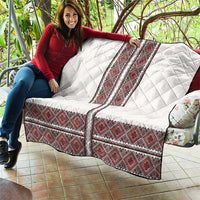 White quilt with red folk embroidery strips and diamond quilting, held on a patio