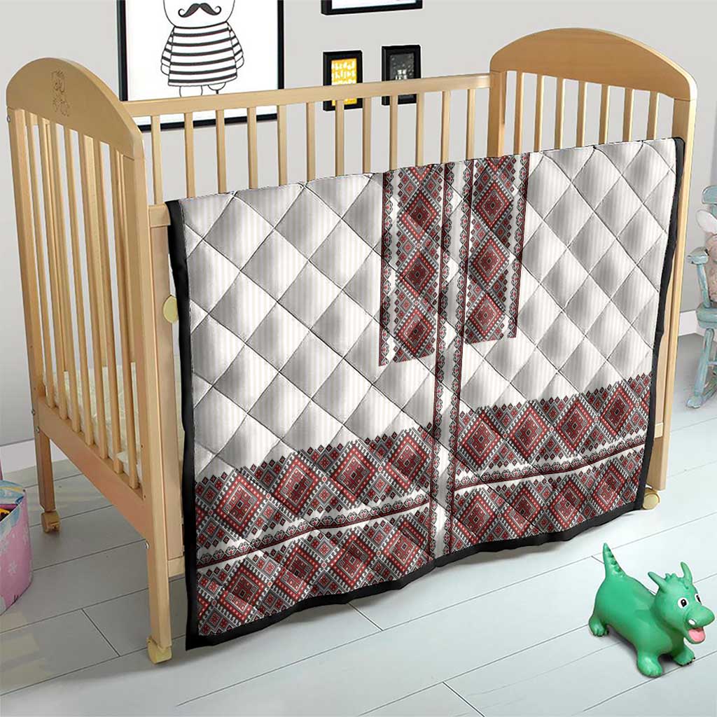 White quilt with red folk embroidery panels and diamond quilting, on a baby bed