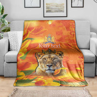 Orange personalized lion blanket with crown emblem and tulip flowers, folded on gray couch