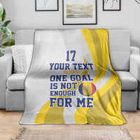 Football blanket on sofa, white with yellow stripes and “ONE GOAL IS NOT ENOUGH” text
