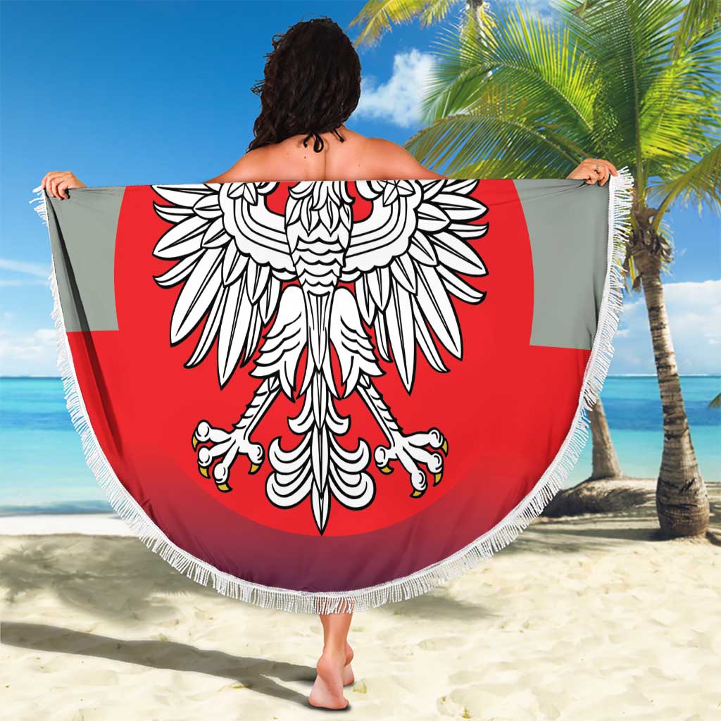 Round beach blanket held open, showing crowned eagle crest on red circle with white border fringe