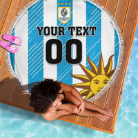 Round beach blanket with blue-and-white stripes, Uruguay crest and sun graphic, fringe trim