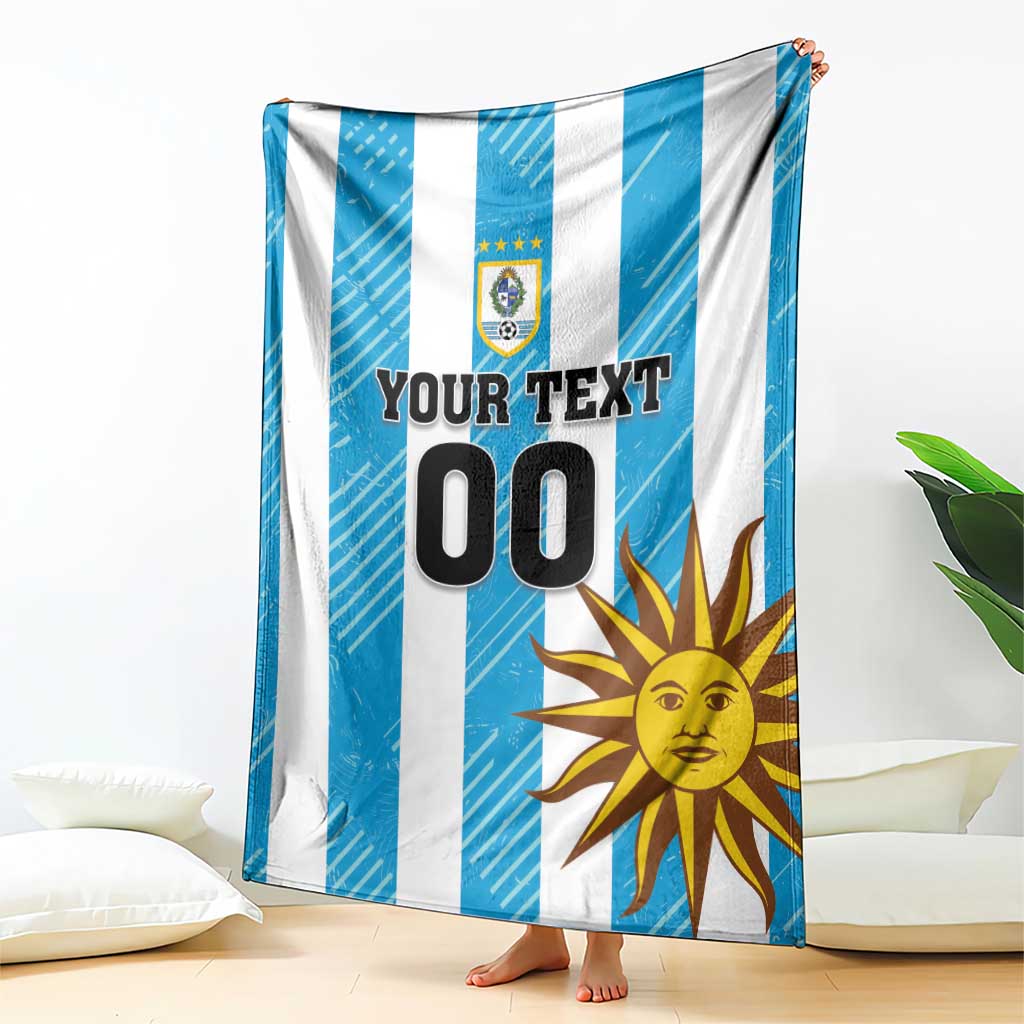 Hanging blue and white striped football blanket with Uruguay crest, sun graphic, and 'YOUR TEXT 00'.
